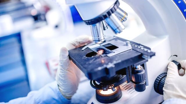 Scientist examining a slide under a microscope in a lab.