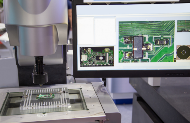 A machine inspecting a circuit board with a computer screen display.